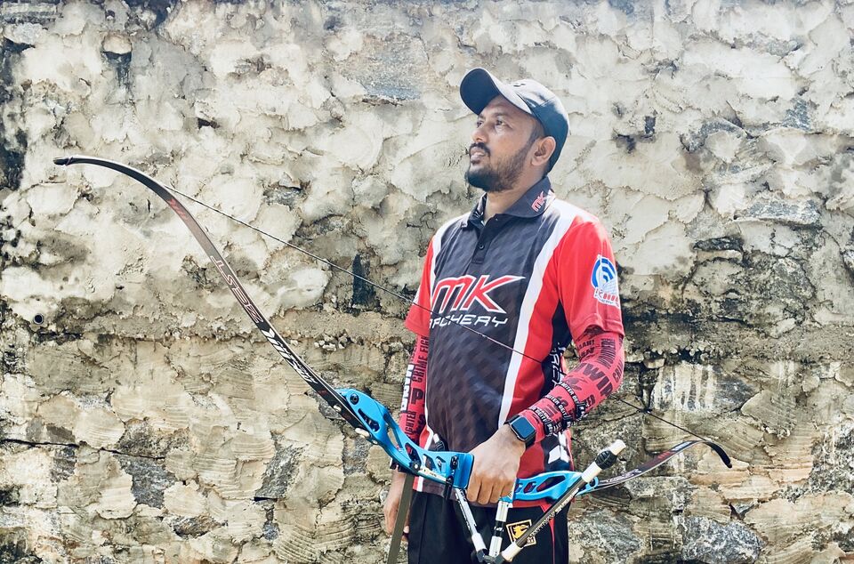 Haneez holding a recurve bow at an archery range, wearing an MK Archery jersey
